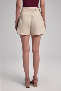 Beige shorts valmistettu kevyestä kankaasta, jossa on korkea vyötärö, takataskut ja rento istuvuus. Sileä pinta ilman näkyviä kuvioita.