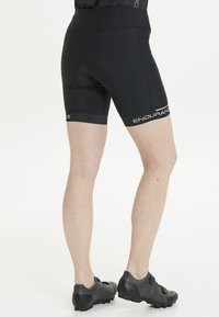 Svarta cykelshorts med en åtsittande design, utrustade med en bred midja och en kontrasterande vit logotyp. Ytan är slät, vilket gör dem idealiska för träningskläder.