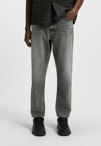 Jeans in denim grigio con vestibilità ampia, design a gamba dritta e una leggera sfumatura. Abbinati a sneakers nere per un look informale.