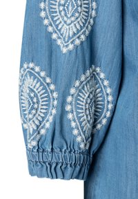 Manica in denim blu con motivi floreali a rombo ricamati in bianco e polsino elasticizzato.