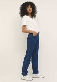 Jean en denim bleu avec poches avant, taille haute et coupe droite. Assorti à un t-shirt blanc à col en V et des baskets blanches.