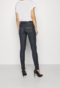 Jeans oscuros y ajustados de mezclilla, con dos bolsillos traseros que presentan detalles de costura sutiles. Combinados con una camiseta blanca y tacones altos negros.