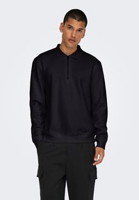 Schwarzer Pullover mit halbem Reißverschluss am Kragen, gerippten Bündchen und Saum. Glatte Textur, lockere Passform und minimalistisches Design.