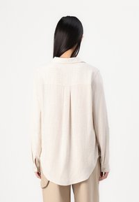 Lichtbeige overhemd met lange mouwen, een button-down kraag, een rugplooidetail en een afgeronde zoom. Gelaagd stof met een iets losse pasvorm.