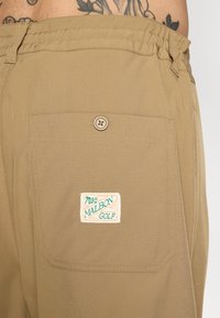 Bež hlače s elastičnom waistline, zatvaranjem na dugme i stražnjim džepom s šarenim logotipom "Malbon Golf".