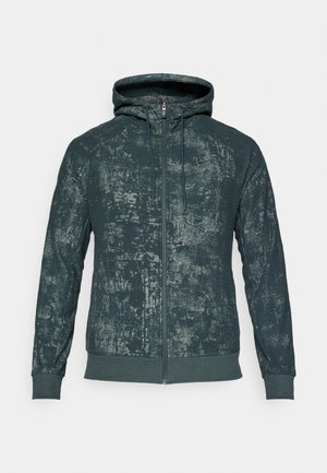 Sweat à capuche zippé en vert foncé avec un motif texturé, doté d'une fermeture éclair sur le devant et de poignets côtelés. Tissu léger.