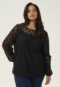 Top lung cu dantelă neagră, cu mâneci lungi și guler cu margini ondulate, model floral și mâneci transparente; croială relaxată cu căptușeală solidă dedesubt.