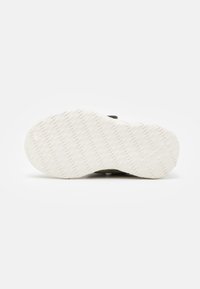 Suela blanca texturizada de una zapatilla con un ligero logo en relieve "hummel" visible cerca del área del talón sobre un fondo liso.
