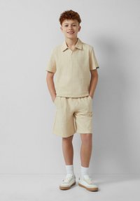 Beige gestreiftes Polohemd mit kurzen Ärmeln und passenden Shorts, aus leichtem Material gefertigt. Weiße Sneakers und Socken runden das Outfit ab.