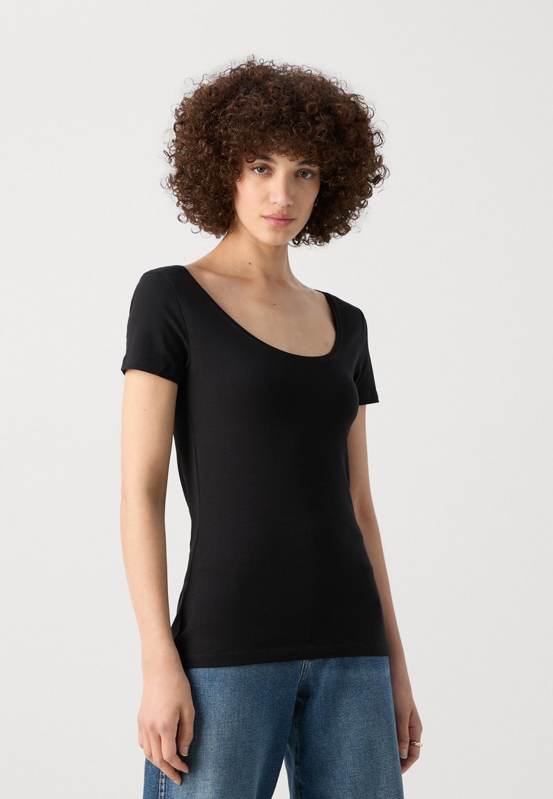 T-shirt noir à manches courtes avec un col rond, design ajusté, texture douce et finition lisse. Associé à un jean en denim bleu clair.