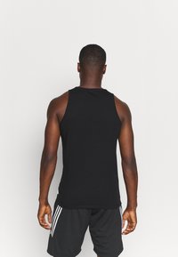 Débardeur noir sans manches en coton, avec un col rond, une texture lisse et un design simple. Porté avec un short noir.