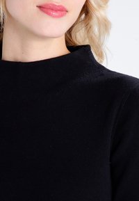Pull à col roulé noir, texture côtelée, design ajusté, tissu doux, col haut avec des détails de couture minimalistes, vue rapprochée de la partie supérieure.