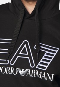 Felpa nera con cappuccio con grandi loghi "EA7" e "emporio ARMANI" ricamati in bianco, con coulisse testurizzate e design classico.