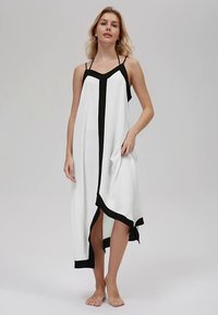 Balta kleita ar melniem akcentiem, plānām lencītēm, asimetrisku apakšmalu un brīvu piegriezumu. Izgatavota no viegla auduma.