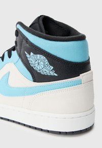 Uvećani prikaz plave, crne i bijele Air Jordan tenisice koja prikazuje krilasti košarkaški logo na ovratniku gležnja.