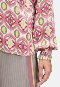 Langarmbluse aus leichtem Stoff mit einem geometrischen Muster in Rosa, Olivgrün und Gelb; geraffte Manschetten und ein leicht abgerundeter Saum.