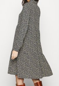 Abito floreale di colore blu scuro con piccoli motivi bianchi e verdi. Presenta maniche lunghe, colletto e una gonna svasata.