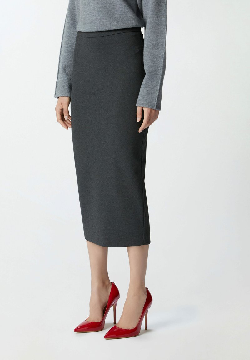 Gonna grigia in tessuto elasticizzato, con vita alta e silhouette aderente, abbinata a tacchi alti rossi lucidi.