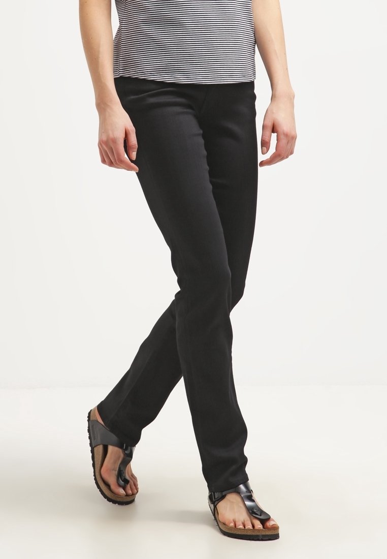 Pantaloni neri slim-fit con un taglio classico, dotati di tasche anteriori e una trama liscia, abbinati a sandali neri piatti su uno sfondo neutro.