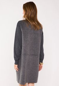 Abito grigio lavorato a maglia con maniche lunghe, un mix di trame morbide, tasche e una silhouette rilassata, con un pannello posteriore di un grigio più scuro.