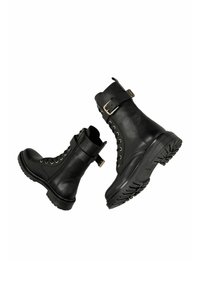 Paire de bottes de combat en cuir noir avec des lacets, des fermetures éclair latérales, des semelles épaisses crantées et des boucles argentées près du haut.