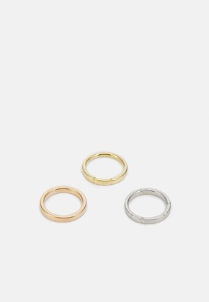 Tre anelli metallici: uno in oro rosa, uno in oro con dettagli in rilievo e uno in argento, tutti con marchi incisi sulla parte interna.