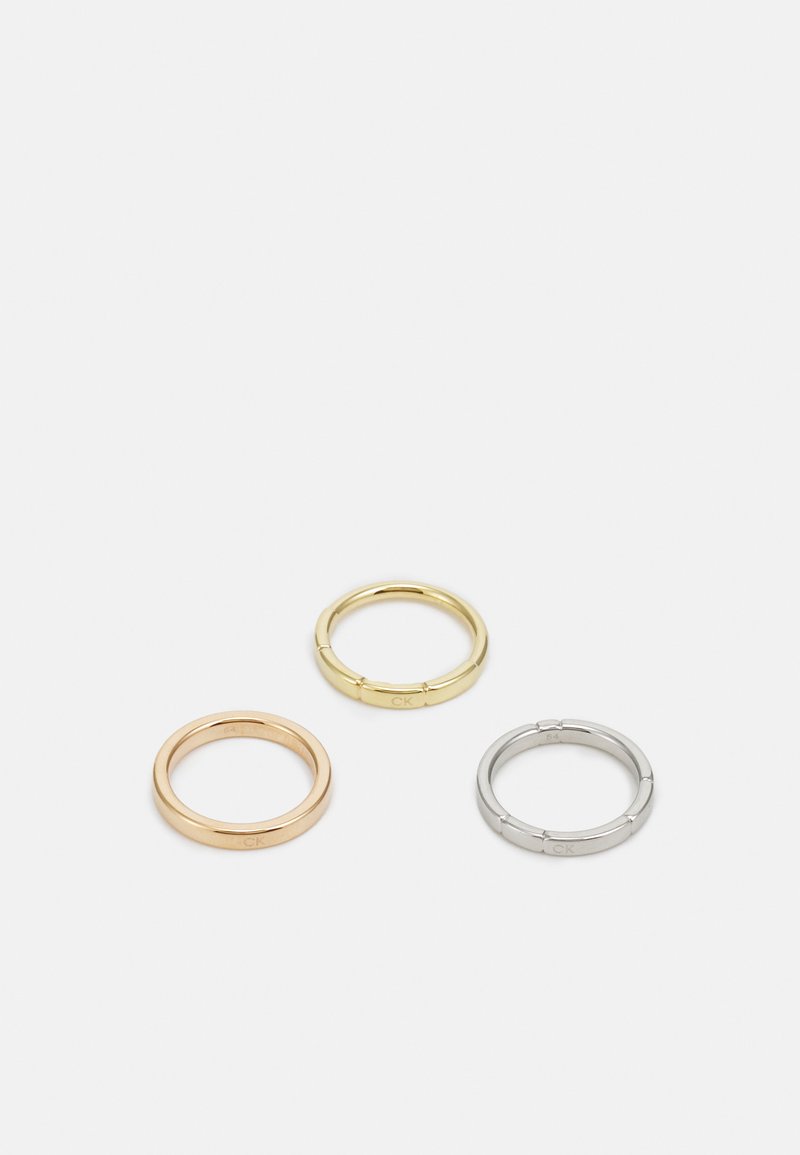 Tre anelli metallici: uno in oro rosa, uno in oro con dettagli in rilievo e uno in argento, tutti con marchi incisi sulla parte interna.