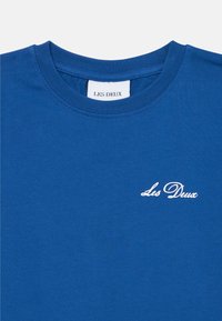Kongelig blå kortermet bomull T-skjorte med rund hals og hvit brodert "Les Deux" logo på venstre bryst. Glatt tekstur.