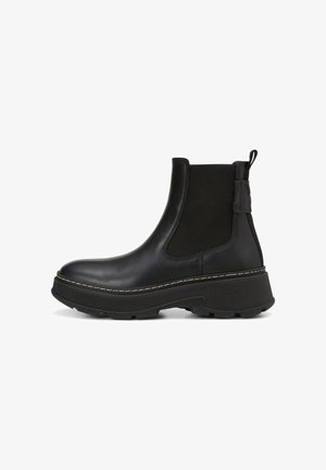 Bottines Chelsea noires avec une semelle épaisse, en cuir lisse, panneaux latéraux élastiques et une languette arrière; détail de couture visible.