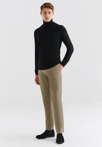 Czarny, dopasowany sweter z golfem zestawiony z jasnobrązowymi, slim-fit spodniami i czarnymi botkami za kostkę. Gładka faktura, minimalistyczny design.