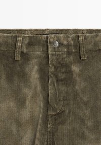 Olivengrønne fløjelsshorts med lodrette ribber, en frontknap med metal detaljer og en tekstureret overflade.