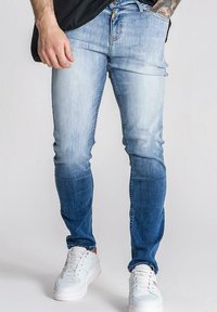 Svijetloplave traperice slim fit kroja s izblijedjelim efektom od tamne do svijetle boje. Nosive su s bijelim, niskim tenisicama.