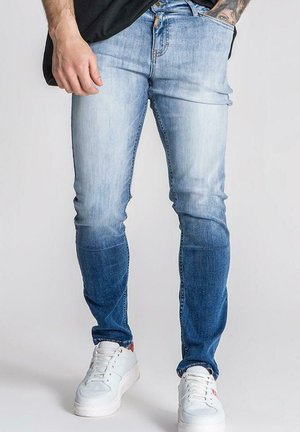 Jeans de mezclilla azul claro con un ajuste slim y desvanecimiento de oscuro a claro. Combinados con zapatillas blancas de corte bajo.