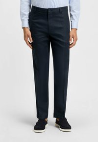 Marineblaues Hosen aus glattem Stoff mit tailliertem Schnitt, flachem Front und einem Knopfverschluss, kombiniert mit dunklen, lässigen Schuhen.