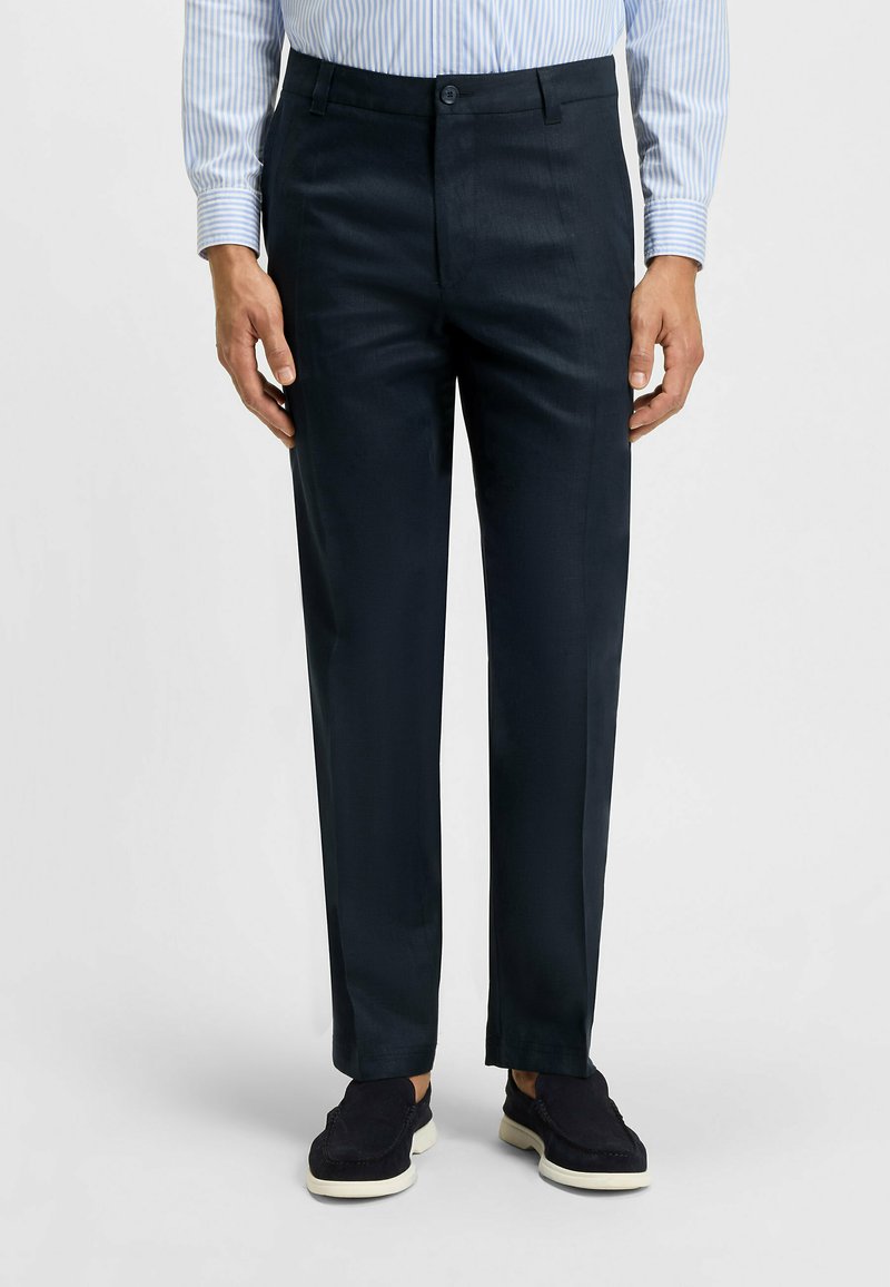 Marineblaues Hosen aus glattem Stoff mit tailliertem Schnitt, flachem Front und einem Knopfverschluss, kombiniert mit dunklen, lässigen Schuhen.