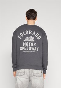 Tmavě šedá mikina s kulatým výstřihem. Na zádech velký bílý potisk: "COLORADO MOTOR SPEEDWAY" s motivem motocyklu.