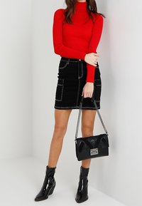 Czerwony prążkowany sweter z golfem, czarna spódnica dżinsowa z kieszeniami, czarne lakierowane botki za kostkę oraz czarna torebka na łańcuszku z ozdobnymi detalami.