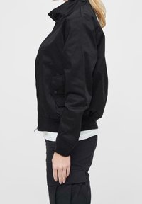 Schwarze Bomberjacke, aus Baumwollmaterial, mit geripptem Kragen, Bündchen und Saum, seitliche Tasche mit Knopfdetail, cropped Design.