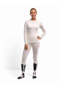 Lichtgrijs, aansluitend shirt met lange mouwen en legging. De legging heeft zwart-grijze accentpatronen op de kuiten. Sokken met zwarte accenten.