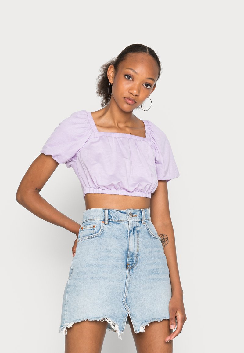 Top lilás cropped com mangas bufantes, decote quadrado e bainha franzida, combinado com uma saia de ganga azul clara com bainha desfiada e fenda frontal.