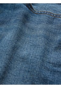 Blå denimtyg med en strukturerad yta, med synliga vävmönster och kontrasterande beige sömmar längs kanterna.