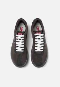 Dark brown sneakers with a mix of smooth and suede textures, white laces, and a red Camper logo on the tongue. Rounded toe and gray soles.