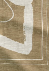 Tissu beige avec une surface texturée présentant des motifs et des lignes abstraits blancs. Le design inclut des formes irrégulières et des bords doux.