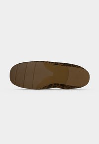 Semelle d’une chaussure plate avec une semelle en caoutchouc marron et un tissu imprimé léopard autour du bord, présentée sur un fond uni.