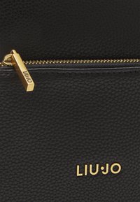 Sort tekstureret læderpung med en guldfarvet lynlås og LIU·JO-logoet præsenteret på en fremtrædende måde.