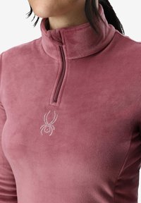 Fleece pullover i støvet rosa med h�øj krave og kvart lynlås. Har et rhinsten-edderkoppelogo på brystet, glat tekstur.
