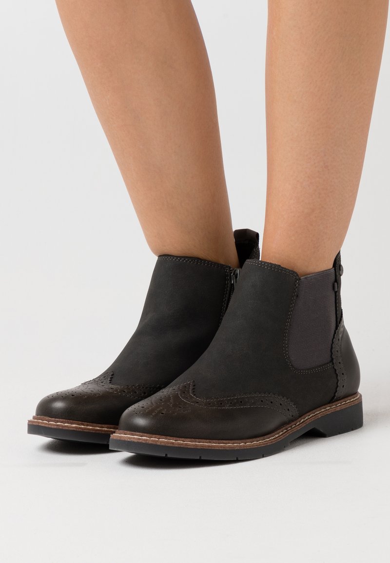 Black leather ankle boots with a brogue detail, elastic side panels, and a low stacked heel. Smooth texture with a slightly matte finish.