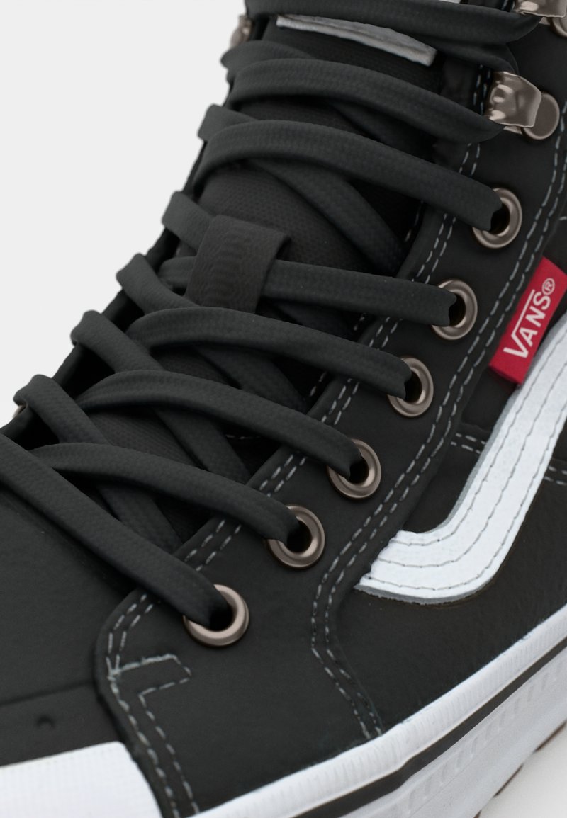 Schwarze High-Top-Sneaker mit Gummisohle, flachen schwarzen Schnürsenkeln, silbernen Ösen und einem weißen Streifendesign. Material texturiert und glatt.