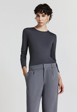 Body grigio a maniche lunghe realizzato in materiale liscio, abbinato a pantaloni grigi su misura con pieghe frontali e tasche oblique.