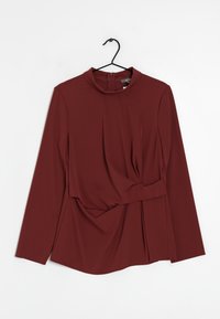 Mörkröd långärmad topp med hög krage, plisserad frontdesign, samlad midjedetalj och subtil lyster. Avslutas med en dragkedja i ryggen.